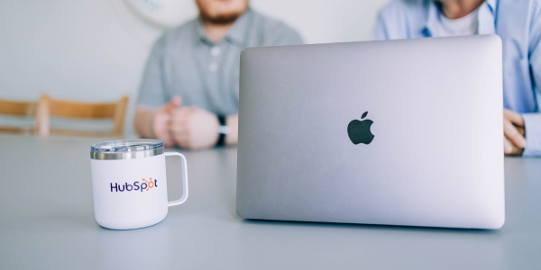 two people sitting in the background with a white mug that reads HubSpot and a laptop