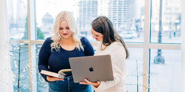 Two people standing in front of a window holding a laptop and a book